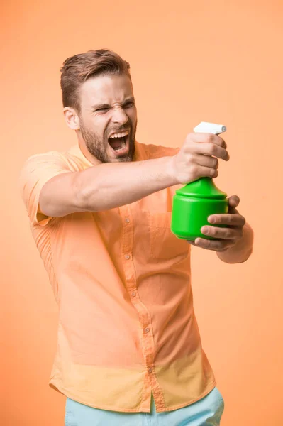 Macho memegang botol semprotan plastik sebagai senjata kuning latar belakang. Pria dengan semprotan air di tangan berpura-pura menembak. Pekerjaan rumah tangga dan konsep sanitasi. Hati-hati dengan pelembab. Konsep pelembab — Stok Foto