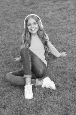 İyi günler. moda ve güzellik. Mutlu çocuklar günü. Bahar tatili zamanı. Yeşil çimlerin üzerinde kaygısız bir çocuk. Küçük kız kulaklık takıyor. Çocuk müzik dinliyor. Okuldan sonra parkta biraz dinlen.