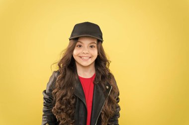 Havalı ve şık. Nasıl hippi olunur. Şık deri ceketli mutlu çocuk. Küçük kız şapka takıyor. Çocuk modası konsepti. Çocuğun uzun kıvırcık saçları var. Kuaföre git. Hip hop tarzında. Çok havalı görünüyorsun.