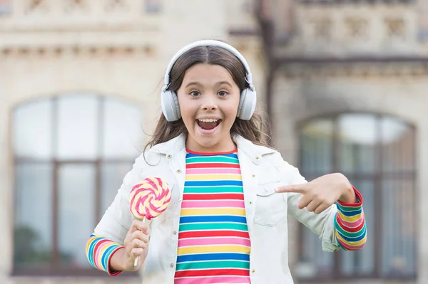 Chica auriculares inalámbricos comen caramelos piruleta, dulce concepto de la infancia — Foto de Stock