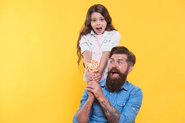 Щаслива сім'я тато і дочка їдять льодяник жовтий фон, солодкий командний концепт — стокове фото