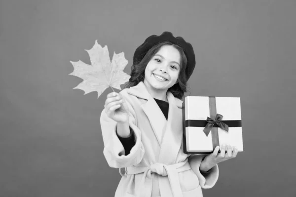 Venta estacional. Oferta de otoño. Niña y caja de regalo. Muchacho lindo cara mantenga hoja de arce. Niño con hoja de otoño recibido presente. Compras de otoño. Viernes Negro. Pequeña niña caída traje rojo fondo — Foto de Stock