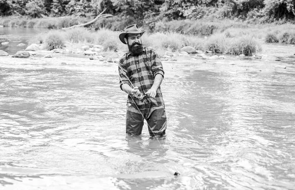 Жорстокий чоловік у гумових чоботях стоїть у річковій воді. Задоволений рибалка. Рибальське чоловіче хобі. Рибальське обладнання. Риба на гачку. Риболовля вимагає від вас бути уважним і повністю присутнім в даний момент — стокове фото