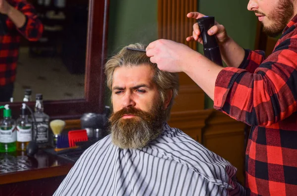 Do not cut your own hair. Hipster client getting haircut. Barber with scissors and client. Barber works on hairstyle for bearded man barbershop background. Guy with long dyed blond hair close up