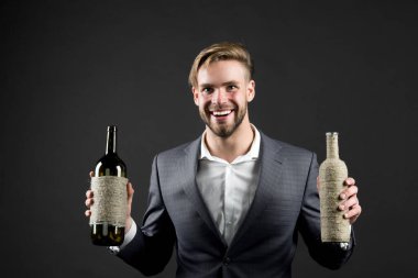 Sommelier 'de iki şişe şarap var. Profesyonel şarap arıtma konsepti. Elinde şarap şişeleri olan resmi takım elbiseli bir adam. Sommelier yakışıklı, esmer arka plandaki neşeli adam. Hangi şarabı seversin?