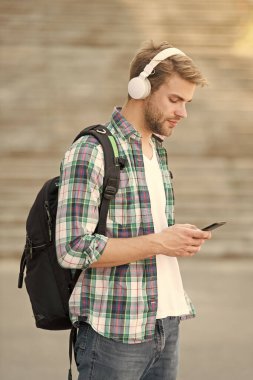 Modayı takip eden adam mesaj yazıyor. Üniversite öğrencisi kulaklıkları akıllı telefon. Online eğitim. Ses kitabı konsepti. Eğitim teknolojisi. Öğrenciyim. Okul hayatı. Müziği dinle. Modern ve dijital gençlik