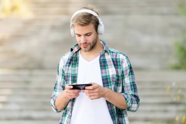 Meşgul adam kablosuz kulaklık kullanıyor, akıllı telefon kullanıyor, oyun konsepti oynuyor