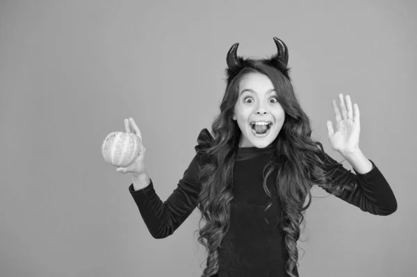 Evil demon. Little demon of child orange background. Happy girl with red demon horns hold pumpkin. Demon is ghouls best friend. Halloween holiday celebration — Stock Photo, Image