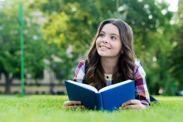 Lassen Sie Ihre kreativen Fähigkeiten untersuchen. Glückliches Kind las Buch auf grünem Gras liegend. Leseförderung. Buch lernen. Schulbibliothek. Literaturstunde. Fantasie und Fantasie. Wissenstag — Stockfoto