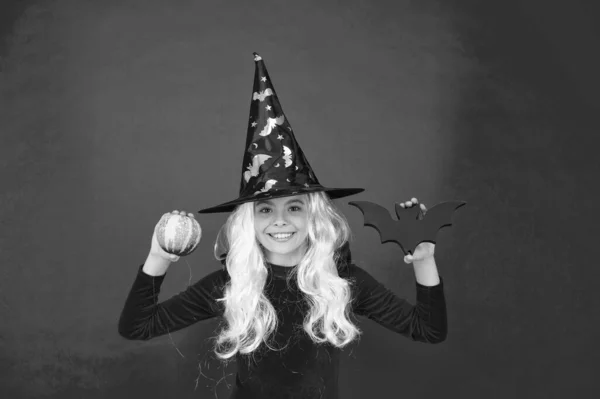 Fábrica de susto. A bruxa segura no taco e na abóbora. A menina usa chapéu de bruxa e cabelo. Menina pequena com olhar de Halloween. Halloween festa menina rosa fundo — Fotografia de Stock