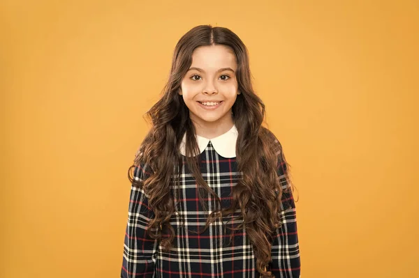 Happy smiling kid portrait. Emotions emotional expression. Just happy. Small girl classy checkered dress. Child long curly hair. Happy schoolgirl stylish uniform. Childhood concept. Kids psychology