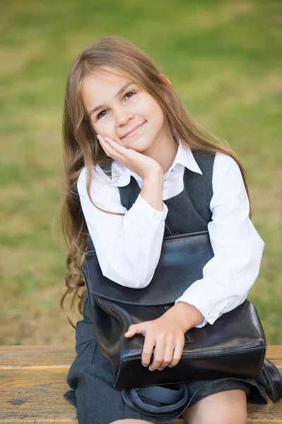 Smart skönhet. Glada barn leende sitter på bänken. En liten flicka håller i en väska i uniform. Skolmode. Skönhetssalong. Tillbaka till skolan. Formell utbildning. 1 september. Kunskapsdag — Stockfoto