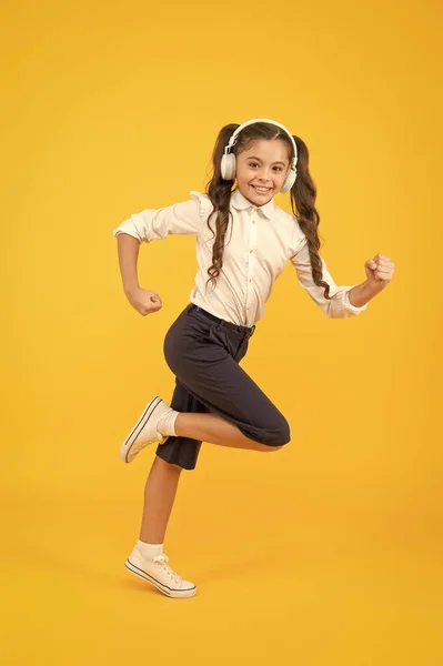 Energetico torna a canzoni scolastiche che ti faranno muovere. Bambino energico sta correndo a scuola su sfondo giallo. Piccola ragazza godendo di musica energica in cuffia. Attivo ed energico — Foto Stock