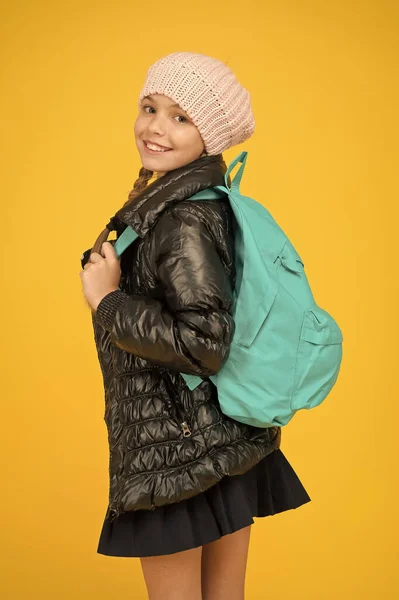 Een mode-outfit voor schoolmeisjes. Kind met rugzak. Modewinkel. Modeconcept. Meisje draagt gebreide muts en jasje met gele achtergrond. Schattige leerling. Herfst herfst winter. Koop kleding voor het schoolseizoen — Stockfoto