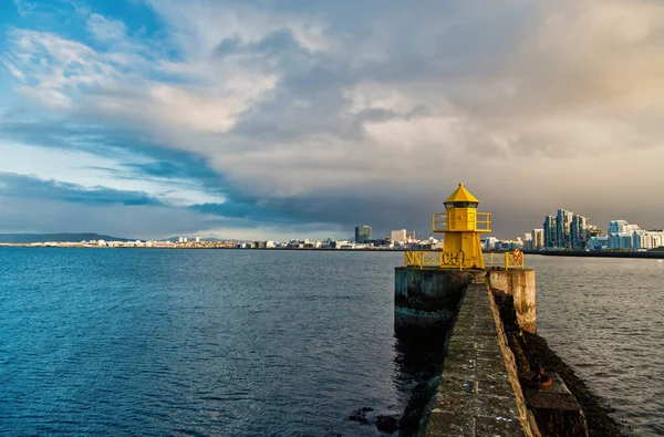 Concetto di navigazione nei porti marittimi. Trasporto marittimo e navigazione. Faro sul molo di mare in Reykjavik ghiacciaio. Faro giallo torre luminosa sulla riva del mare. Paesaggio marino e skyline con faro luminoso — Foto Stock