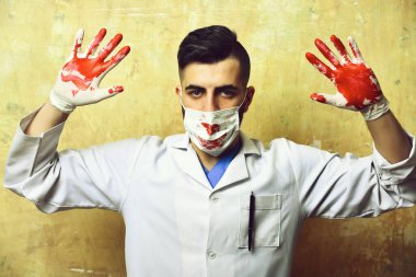 Kanlı elleri havada, ameliyat maskeli doktor.