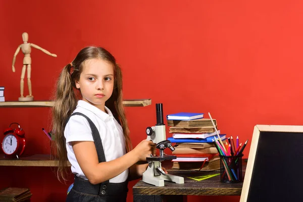 Kırmızı duvar arkasında çocuk ve okul malzemeleri var.