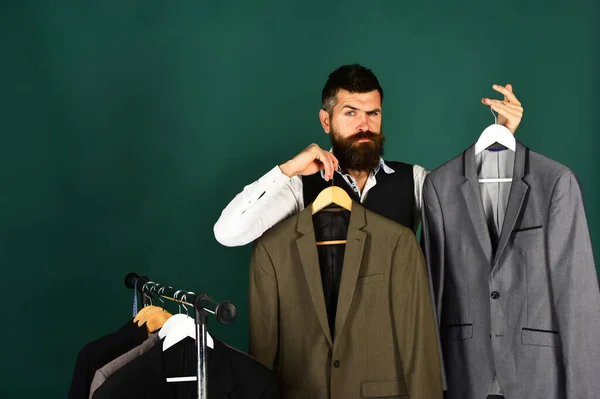 Man with beard by clothes rack. Tailor with confused face