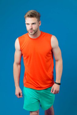 Seksi kaslı vücutlu bir sporcu. Maraton, spor ve spor konseptinden önce koşuculuk eğitimi. Süslü sakallı, turuncu yelek ve mavi şort giyen bir adam. Sporcu mor arkaplanda izole edildi