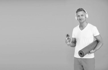 Su alımı susuzluğa iyi gelir. Sporcu su şişesini ve yoga minderini mavi arka planda tutar. Susuzluk ve susuzluk. Egzersiz sırasında susuzluk ve içki. Susuzluktan kaçınmak için su iç, boşluğu kopyala