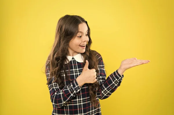 Ses cheveux sont parfaits. présentant le produit pour les cheveux. Petite beauté longs cheveux bouclés. uniforme scolaire élégant pour les enfants. beauté des cheveux sains. bonne enfance. petit modèle de mode mur jaune. espace de copie. — Photo