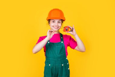 Burası benim yerim. Çocuk müteahhit kask takıyor. Şapkalı ve üniformalı genç kız. Bina ve inşaat. Onarım konsepti. Küçük kız bir mezura kullanıyor. Mühendis. Mutlu çocuk mezurayı tut
