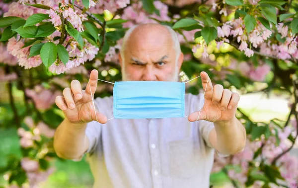 Humor de primavera. cuida da tua saúde. homem com máscara protectora. cheirar flores florescendo em quarentena coronavírus. observar precauções durante a pandemia. vida saudável. tira a máscara no parque sakura rosa florescente — Fotografia de Stock