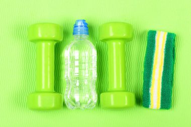 İki plastik halter, bileklik ve şişe. Parlak arkaplanda el ağırlıkları kümesi