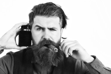 Sakallı adam puro içiyor, ciddi bir yüzü var, parfüm tutuyor.