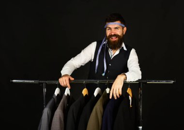 Tasarımcı elbise askılarına yaslanır. Mutlu yüzlü terzi.