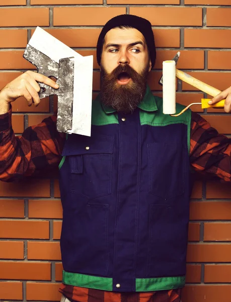 Бородатый мастер держит различные строительные инструменты с довольным лицом — стоковое фото
