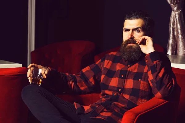 Hombre barbudo hipster sosteniendo vaso de whisky en silla roja — Foto de Stock