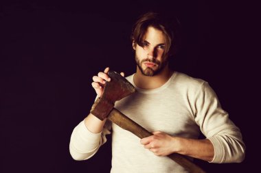 Sakallı ve dikkatli bakışlı adam yaşlı paslı baltayı tutuyor.