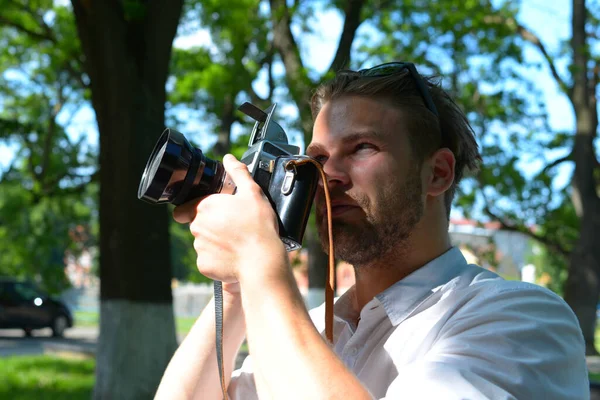 Man with beard holds photocamera on green park background — Stock Photo, Image