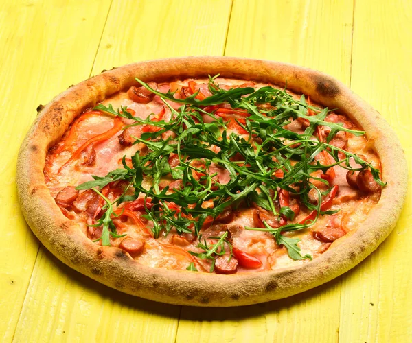 Pizza med bacon, ost och ruccola på trä gul bakgrund — Stockfoto