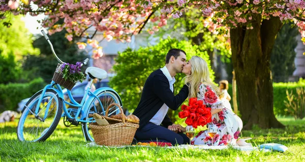 Älskar allt med henne. njuta av naturen tillsammans. ha picknick i stadsparken. man och kvinna koppla av med mat korg. Romantiskt par under Sakura Blossom träd. par kär i grönt gräs — Stockfoto