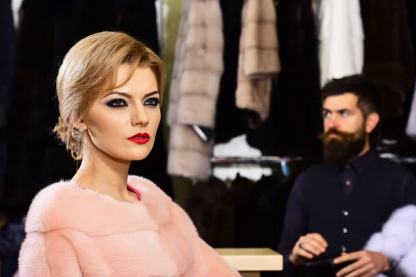 Woman in pink fur coat with bearded man in shop.