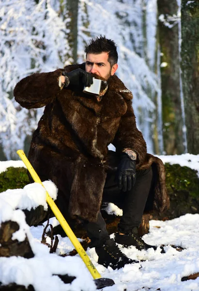 Mannen i päls dricker ur en metallkolv. Brutal gameeper. — Stockfoto