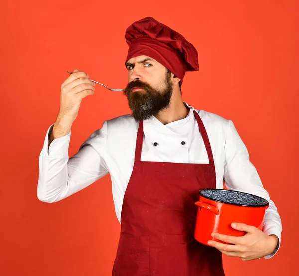 Homem com barba segura utensílios de cozinha no fundo vermelho. — Fotografia de Stock