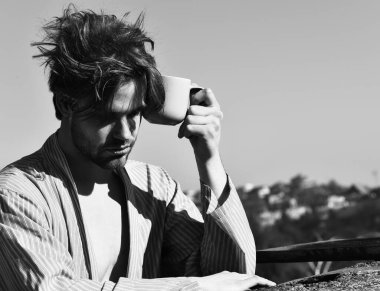 Mavi çizgili pijamalı, elinde fincanla beyaz maço.