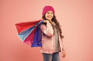 Alışverişte gündelik görünüşünü geliştir. Alışveriş torbalarını tutan mutlu kız. Küçük çocuk alışverişi sever. Şirin, küçük, pembe bir arka plan. Sonbahar indirimi. Alışveriş onun hayatı.