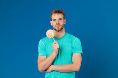 Lolipop eğlencesi. Adam kocaman renkli lolipop yiyor. Tüylü adam lolipopu seviyor. Yemek konseptini aldatmak. Şeker sağlığa zararlıdır. Adamın elinde lolipop şeker menekşesi var. Çocukluk tadı