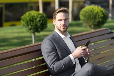 Adam parkta akıllı telefon kullanıyor. Güneşli açık havada cep telefonlu bir müdür. Mavi takım elbiseli iş adamı bankta oturur. Modern hayat ve iş hayatı. İş iletişimi, yeni teknoloji ve mesajlar