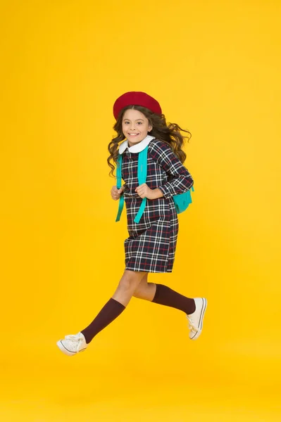 Stylische Teenager College Student Springen. kleines Mädchen mit Rucksack auf dem Weg zur Schule. Bildungskonzept. Schule und Mode. Kind in Schuluniform. Kind in französischer Baskenmütze auf gelbem Hintergrund. Beeilen Sie sich — Stockfoto