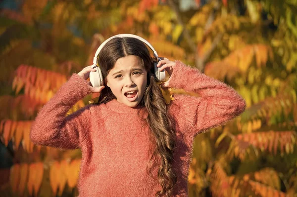 Słuchanie audio w najlepszy sposób pomaga dziecku poprawić słownictwo. Kid girl relaks w pobliżu jesiennego drzewa ze słuchawkami. Jesienne spacery z ładnymi piosenkami. Muzyka na jesienny nastrój. Słuchanie piosenki. Ciesz się muzyką jesienią — Zdjęcie stockowe