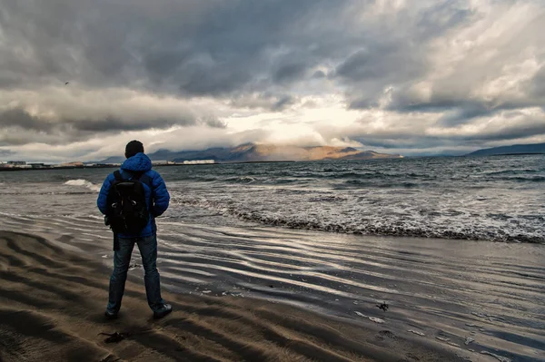 El hombre mira en el horizonte con el paisaje marino reykjavik en la tierra de hielo. concepto de metas futuras. amantes de la naturaleza. viajar y vagabundear. hombre en la orilla del mar mirar en el paisaje marino de pie cerca del agua. cielo dramático en iceland — Foto de Stock