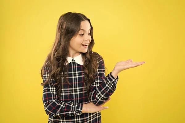 Look here. Product presentation. Small girl nice hairstyle. Child long curly hair. Happy schoolgirl stylish uniform. Happy childhood concept. Happy smiling kid portrait. Emotions emotional expression