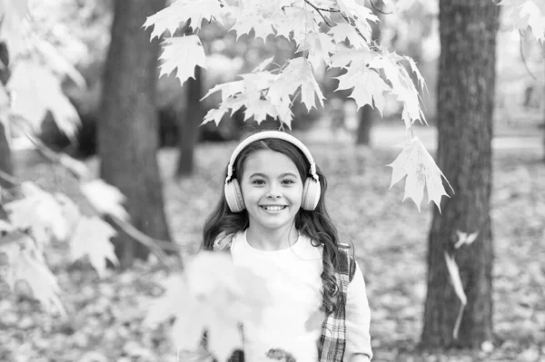 Spadające liście. Szczęśliwa dziewczynka nosić słuchawki jesienne tło natury. Uczennica słuchająca nowoczesnych słuchawek. Technologia słuchawek. Słodki dziecięcy uśmiech ze słuchawkami stereo. Melodia jesieni — Zdjęcie stockowe