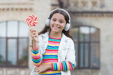 Kablosuz kız kulaklıkları lolipop şekeri yiyor, sevimli çocuk konsepti.