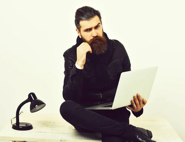 Бородатый брутальный кавказский хипстер сидит за столом с ноутбуком — стоковое фото
